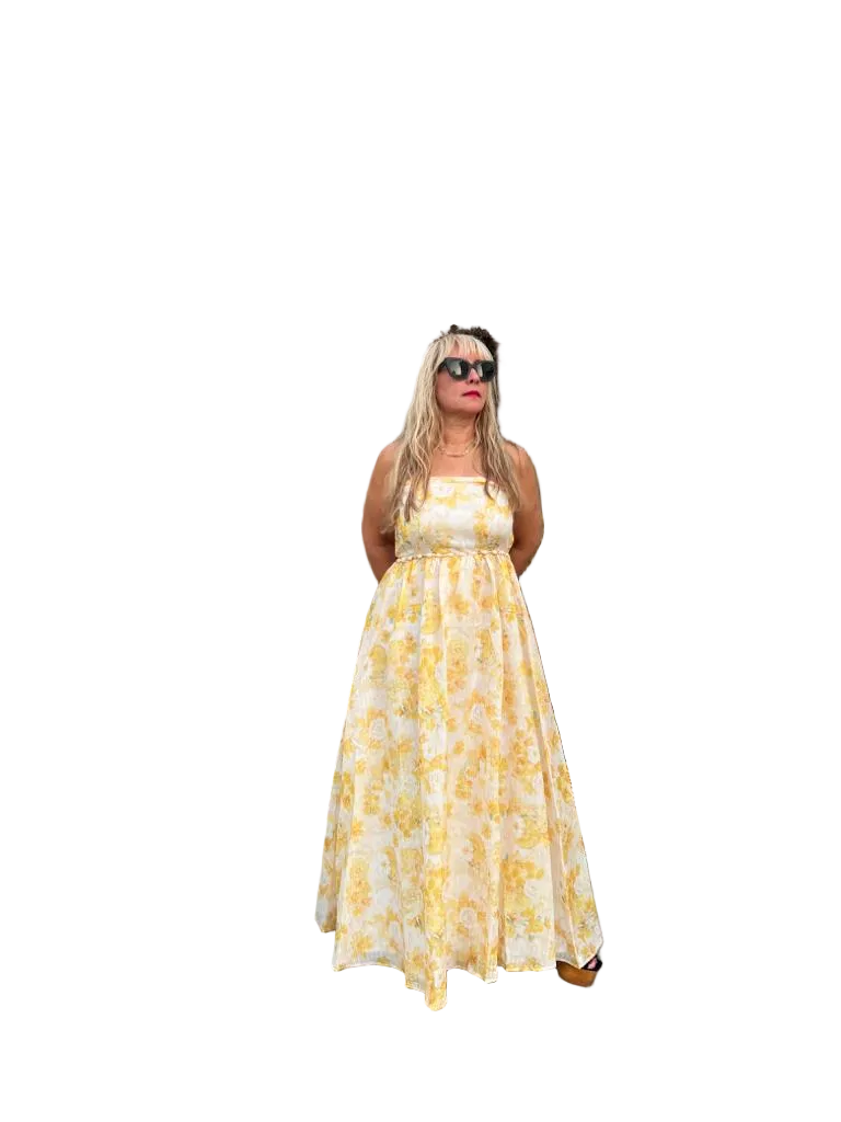 A woman modeling a sleeveless, floor-length yellow and white floral print maxi dress against a solid white background.